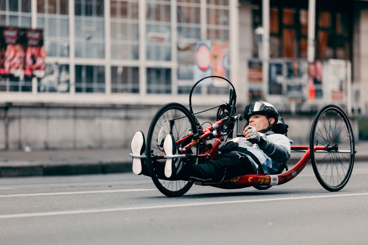 A competitive cyclist using an adaptive handcycle races down a city street, showcasing determination and speed.